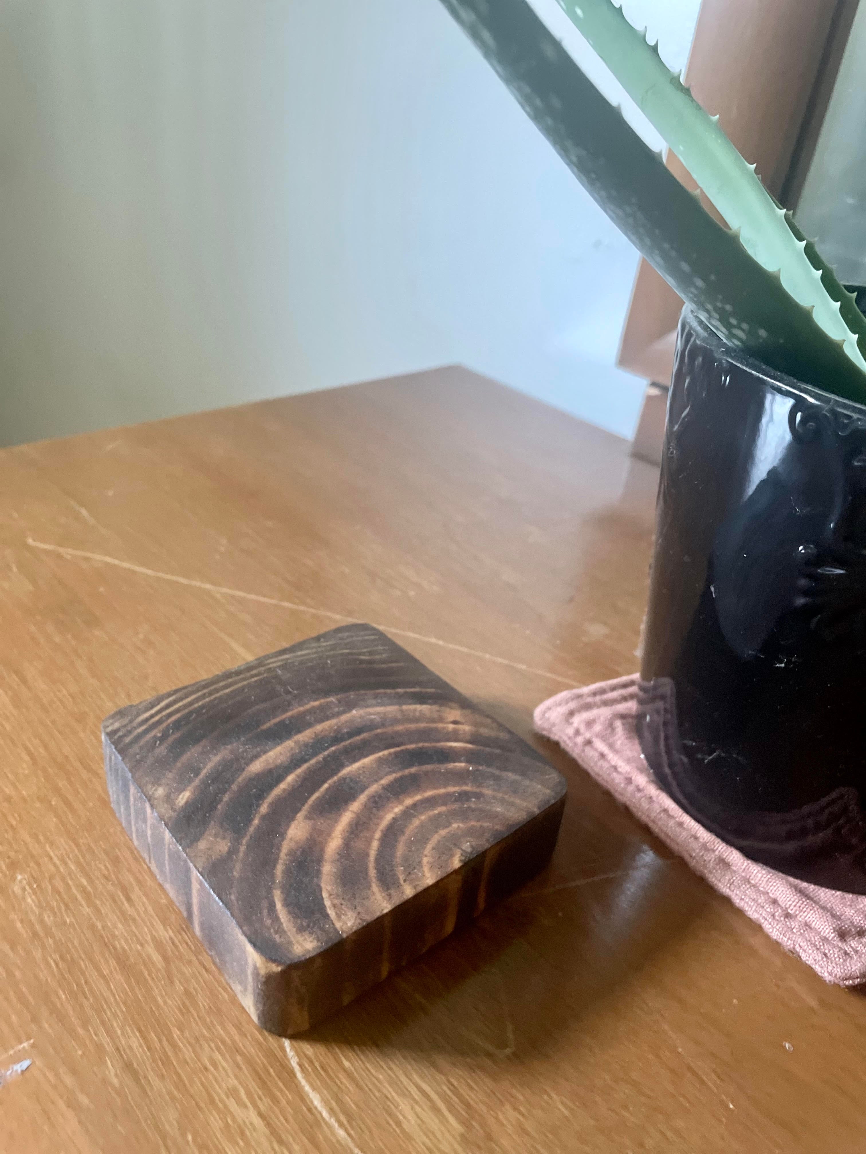 Wooden coaster with circular patterns next to a black mug on a wooden. The black mug is likely a good old fashioned Cup O' Joe.