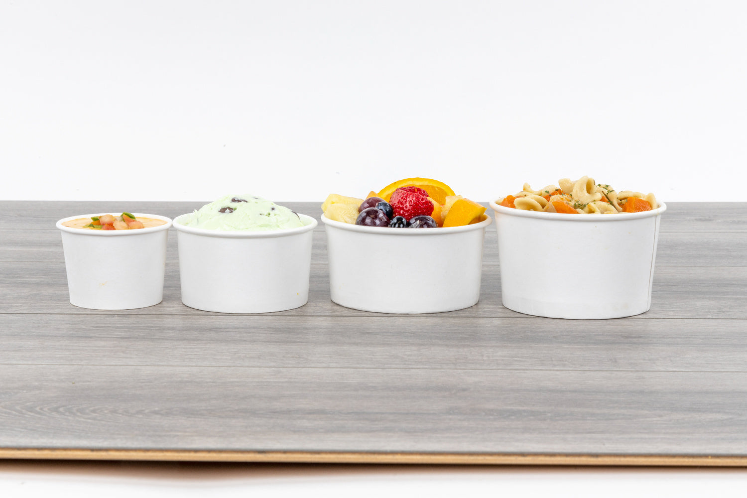 Five small white containers with various fruits on a wooden surface